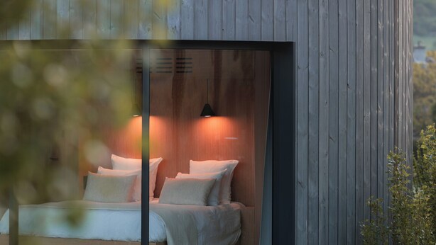 Una estructura de madera moderna y circular con una cama en su interior, rodeada por una zona cubierta de césped.