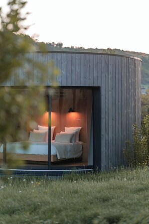 Una estructura de madera moderna y circular con una cama en su interior, rodeada por una zona cubierta de césped.