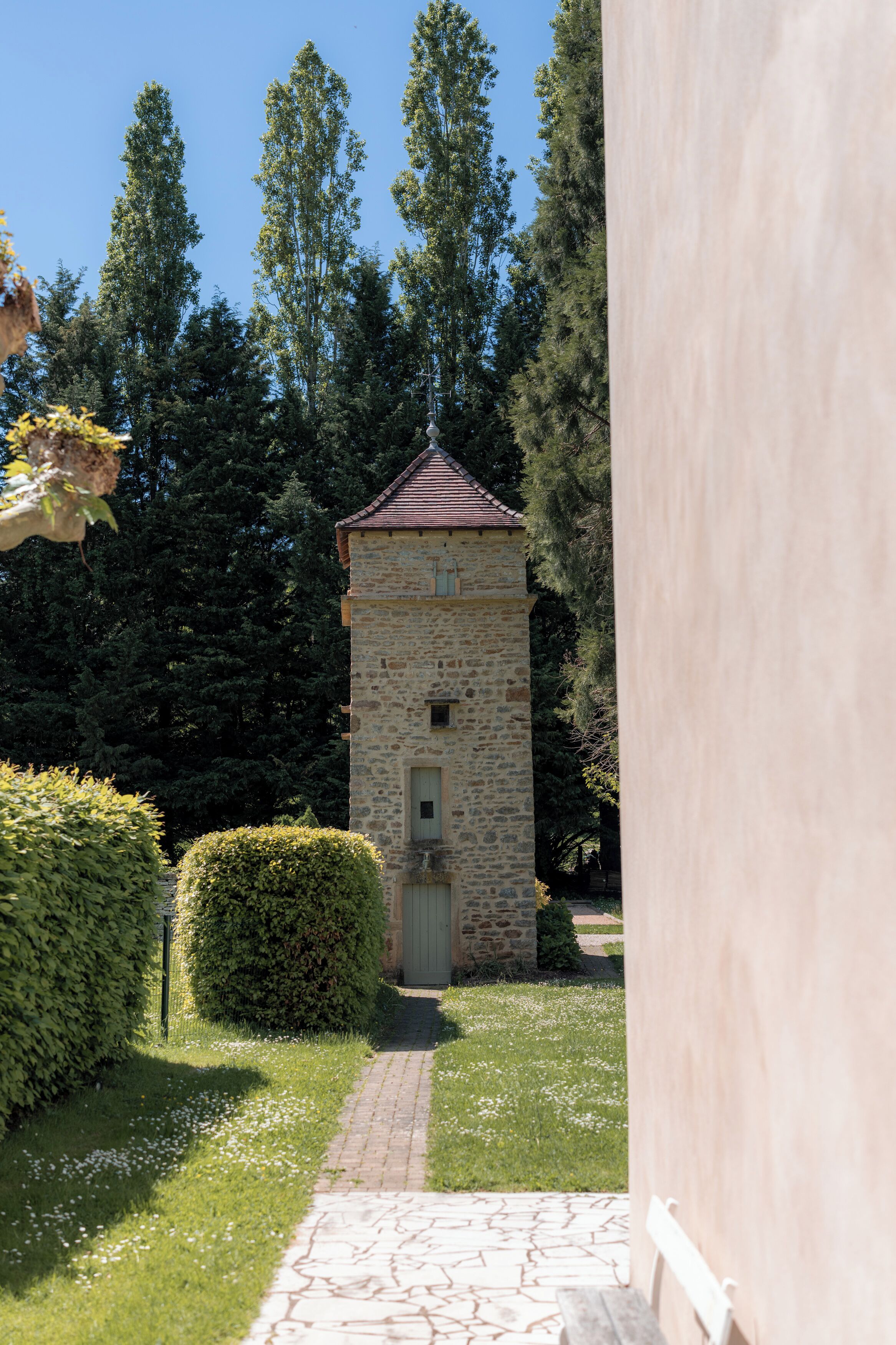 Un bâtiment en pierre, doté d’un toit en tuiles, entouré de verdure et bordé d’un chemin pavé.