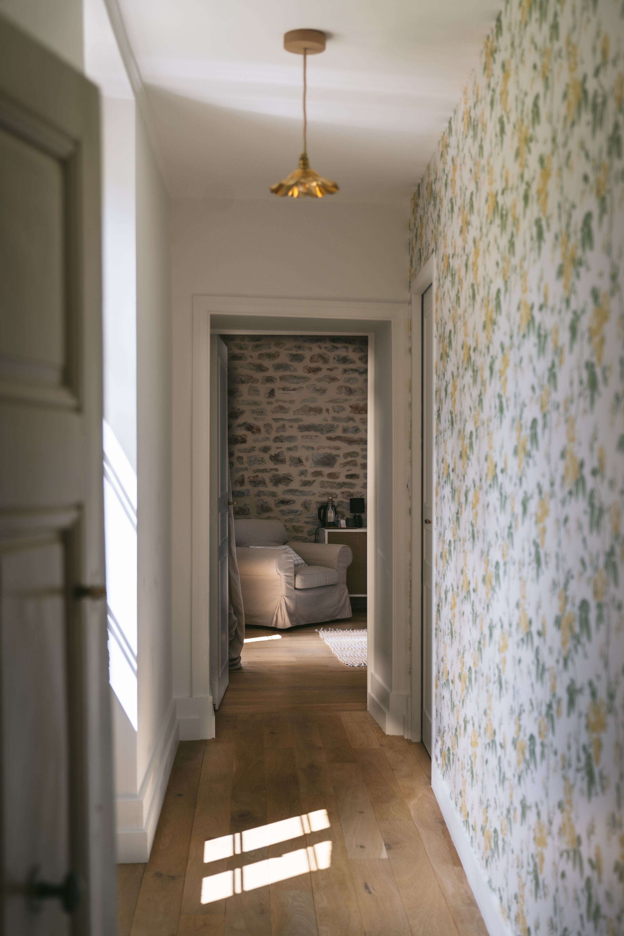 A hallway with wooden flooring, a stone wall, and a patterned wallpaper.