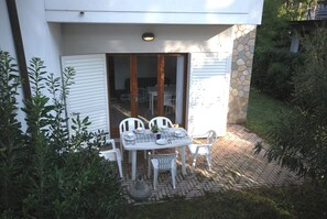 An outdoor patio with a table and chairs, surrounded by plants and a stone wall.