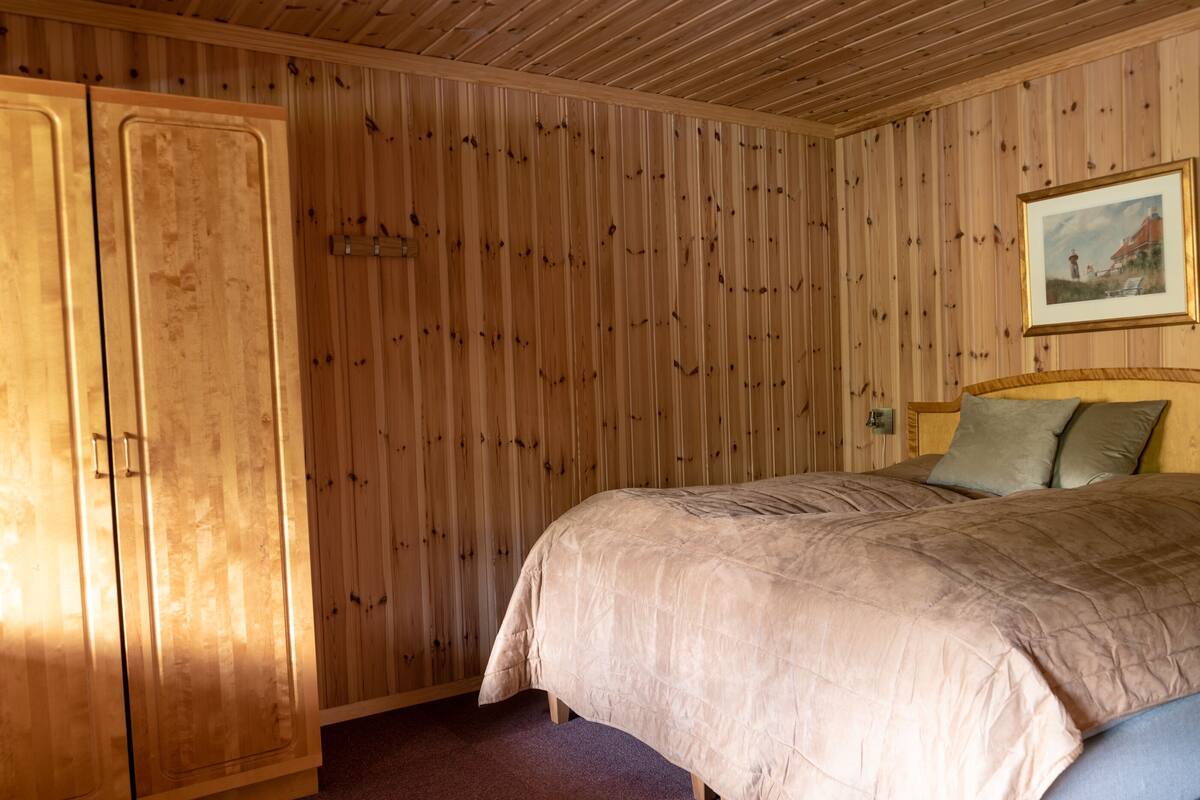 A bedroom with wooden panel walls, a bed with a beige duvet, and a wooden wardrobe.