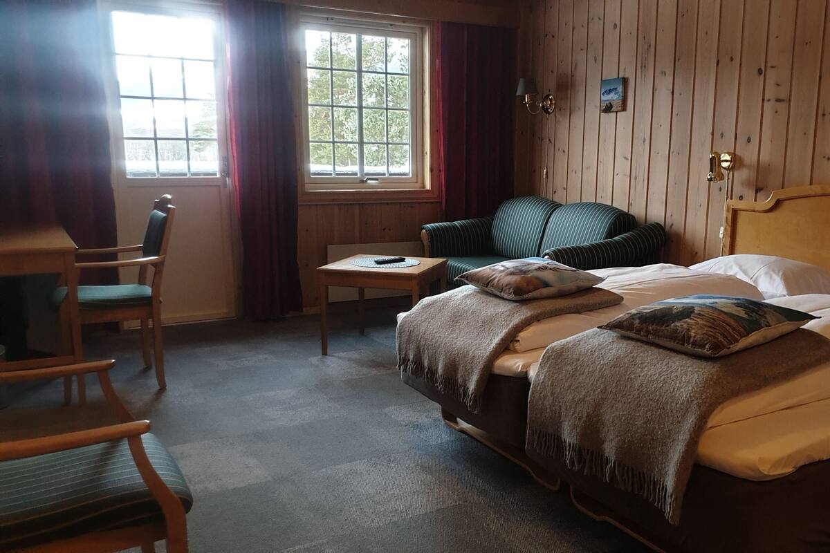 A cozy room with a bed, a chair, a small table, and a window with curtains.