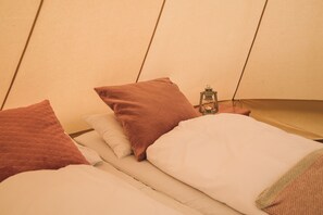 A bed with a white and brown quilt, a white pillow, and a lantern on the side.