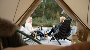 Zwei Personen sitzen in einem Zelt, zwischen ihnen steht ein Tisch, und sie halten Getränke in der Hand.