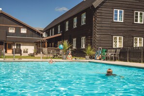 A swimming pool area with wooden cabins in the background.