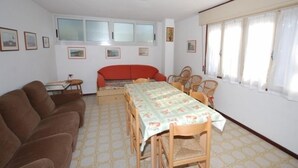 A living room with a sofa set, a dining table with chairs, a red couch, and a window with curtains. - Villa Tiziana (Lignano Sabbiadoro)