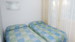 A small room with two beds, a mirror, and a window with curtains. - Villa Tiziana (Lignano Sabbiadoro)