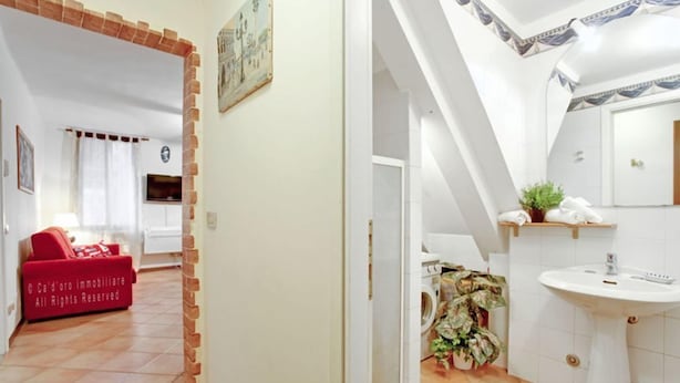 A modern apartment with a red sofa, a washing machine, and a white sink. - Grimaldi Apartments - Lionello (Venice)
