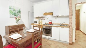A compact kitchen with white cabinets, a wooden dining table, and a red chair. - Grimaldi Apartments - Lionello (Venice)
