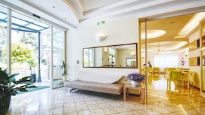 A hotel lobby with a seating area, a large mirror, and a dining area visible through glass doors. - Europa (Cervia)