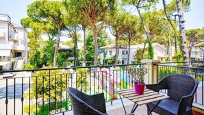 A balcony with wicker chairs and a small table, overlooking a residential area with trees and houses. - Europa (Cervia)