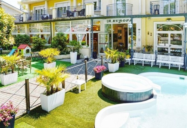 A courtyard with a hot tub, potted plants, outdoor seating, and a building with a sign reading "EUROPA". - Europa (Cervia)