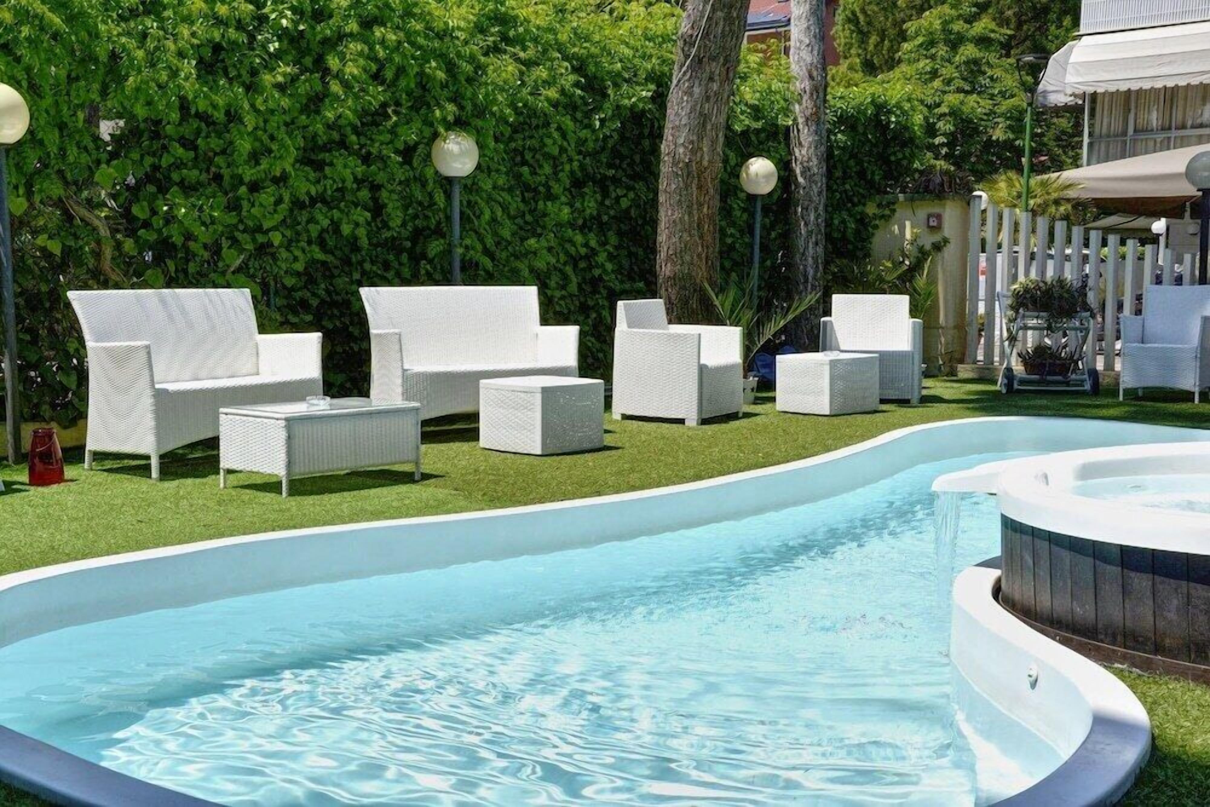 A swimming pool with white lounge chairs and a hot tub.