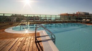 A rooftop pool with clear blue water, wooden deck, and lounge chairs. - Hotel Universal (Cattolica)