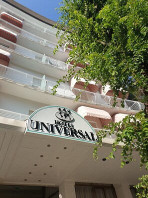 Cartel de hotel con balcones y un árbol al frente.