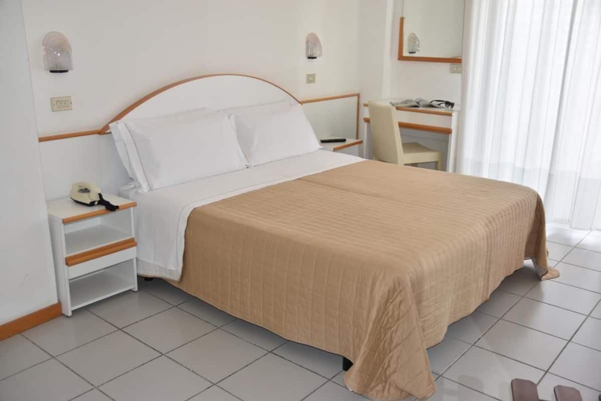 A neatly arranged hotel room with a bed, a desk, a chair, and a small shelf.