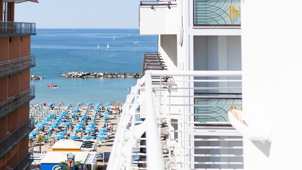 A hotel balcony overlooking a beach with sun loungers and a view of the sea. - Hotel Universal (Cattolica)