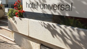 A sign for 'hotel universal' with a modern design, located on a paved area with a metal grate and potted plants nearby. - Hotel Universal (Cattolica)