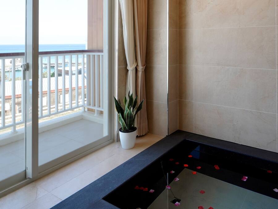 A modern bathroom with a glass-enclosed jacuzzi, a potted plant, and a view of the sea.
