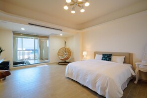 A spacious bedroom with a large bed, a sitting chair, a nightstand, and a view through a glass door. - Little Piggy B&B (Hengchun)