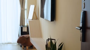 Un salon moderne avec un plancher en bois, une plante en pot, un canapé, un téléviseur fixé au mur et une fenêtre avec des rideaux.