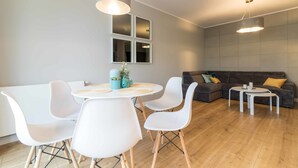 A modern living room with a round dining table, white chairs, a grey sofa, and a grey wall with a mirror. - Dream Holiday Apartament (Gdansk)