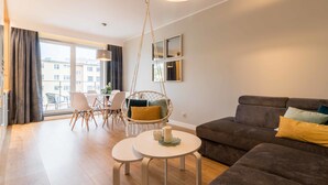 A modern living room with a sofa, two small tables, a hanging chair, and a dining area with chairs and a table. - Dream Holiday Apartament (Gdansk)