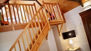 Una escalera de madera que lleva a un nivel superior, un televisor de pantalla plana montado en la pared y una pequeña mesa con una lámpara.