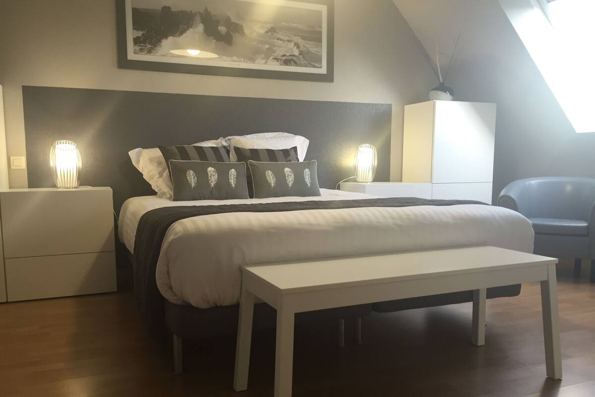 Ett sovrum med en säng, sängbord, en bänk, en garderob och en inramad tavla på väggen.