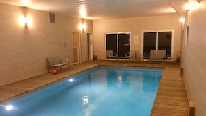 Una piscina cubierta con terraza de madera, sillas y una red de voleibol.