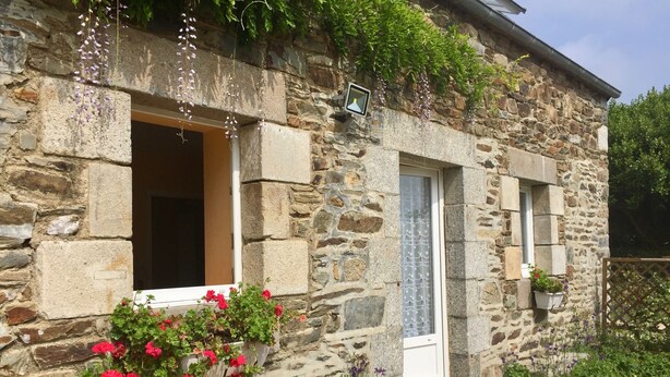 Un edificio de piedra con una ventana y una puerta, una lámpara colgante y una jardinera con flores rojas.