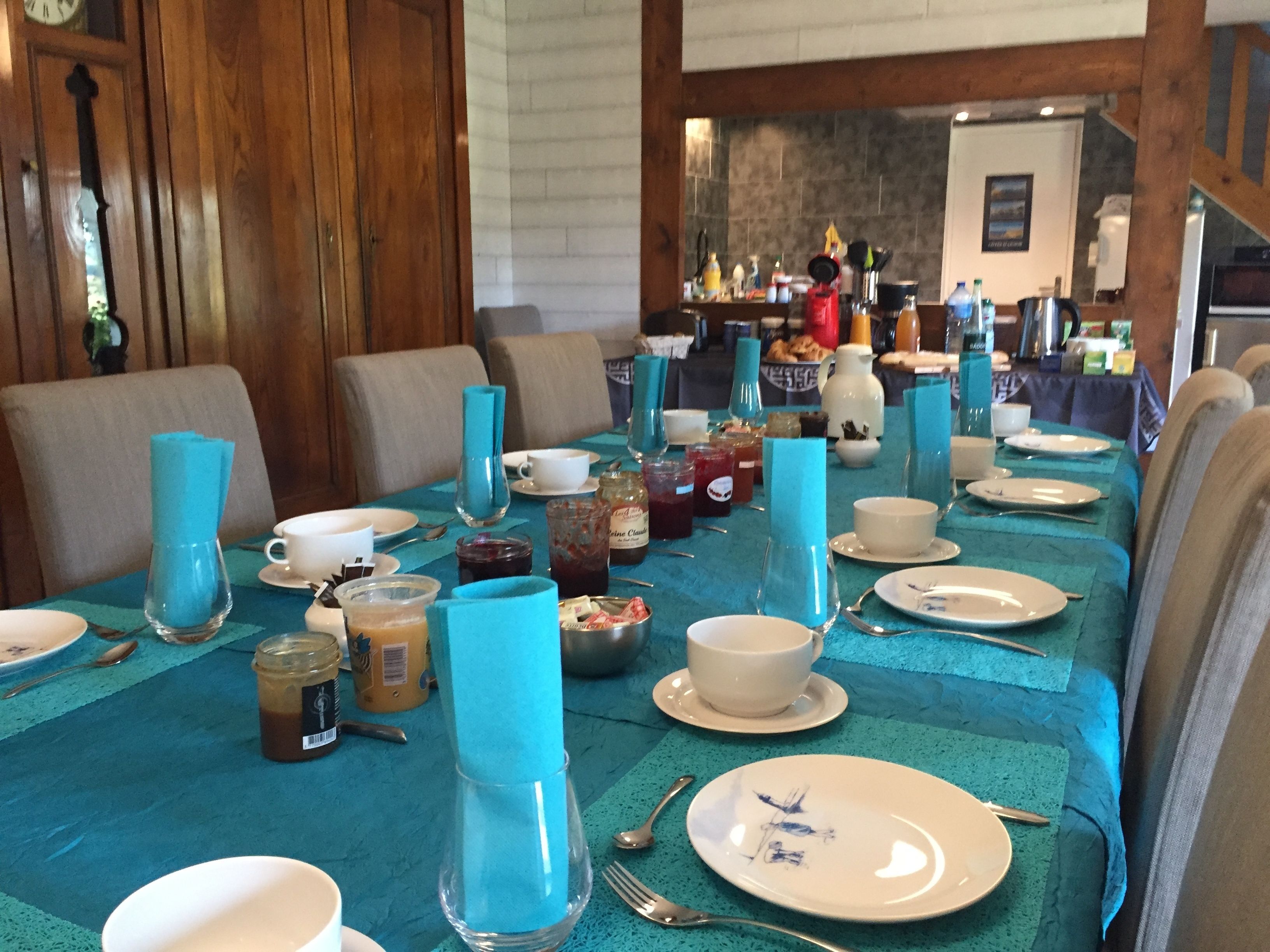 A dining area with a long table set for a meal, featuring blue tablecloths, white plates, and various condiments.