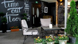 Un área de descanso con una pared decorada con frases motivacionales, un espacio de asiento con una mesa y sillas, y plantas en macetas.