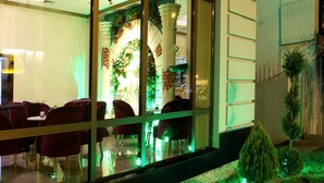 Un restaurante con sillas tapizadas de rojo, una partición de vidrio y vistas al interior iluminado en verde.
