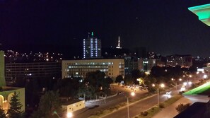 A nighttime cityscape with illuminated buildings, a prominent tower, and a well-lit road with parked cars. - Cron Palace Tbilisi (T'bilisi)
