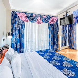 A hotel room with a bed, curtains, a flat-screen TV, and a window with blinds. - Cron Palace Tbilisi (T'bilisi)