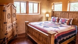 Een houten bed met een sprei, een houten kledingkast en twee ramen.