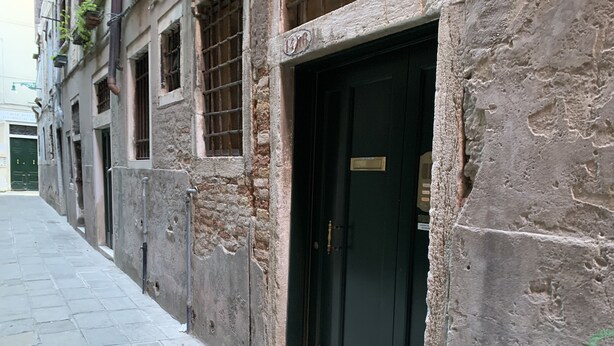 A narrow alley with a row of old buildings, each with a black door and a small window. - Grimaldi Apartments - Casa di Emma (Venice)