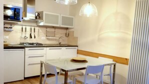 A modern kitchen with white cabinets, a dining table with chairs, and pendant lights. - Grimaldi Apartments - Casa di Emma (Venice)