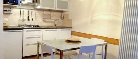 A modern kitchen with white cabinets, a dining table with chairs, and pendant lights.