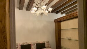 A cozy room with a wooden ceiling, a floral sofa with two pillows, and a glass shelf unit. - Grimaldi Apartments - Casa di Emma (Venice)