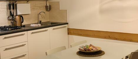 Une cuisine moderne avec des meubles blancs, un évier en acier inoxydable et une cuisinière à gaz. On y trouve une table blanche, une assiette de nourriture et deux chaises.