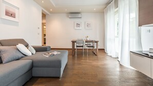 A modern living room with a grey sectional sofa, a dining table with chairs, and a kitchen area with a refrigerator. - Emilia Suite Life (Modena)