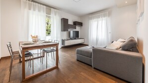 A modern living room with a wooden dining table, grey sofa, and a flat-screen TV on a white cabinet. - Emilia Suite Life (Modena)