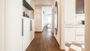 A modern kitchen with white cabinets, a wooden floor, and a dining area in the background. - Emilia Suite Life (Modena)