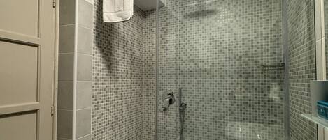 A bathroom with a glass shower enclosure, a white sink, and a tiled shower wall.