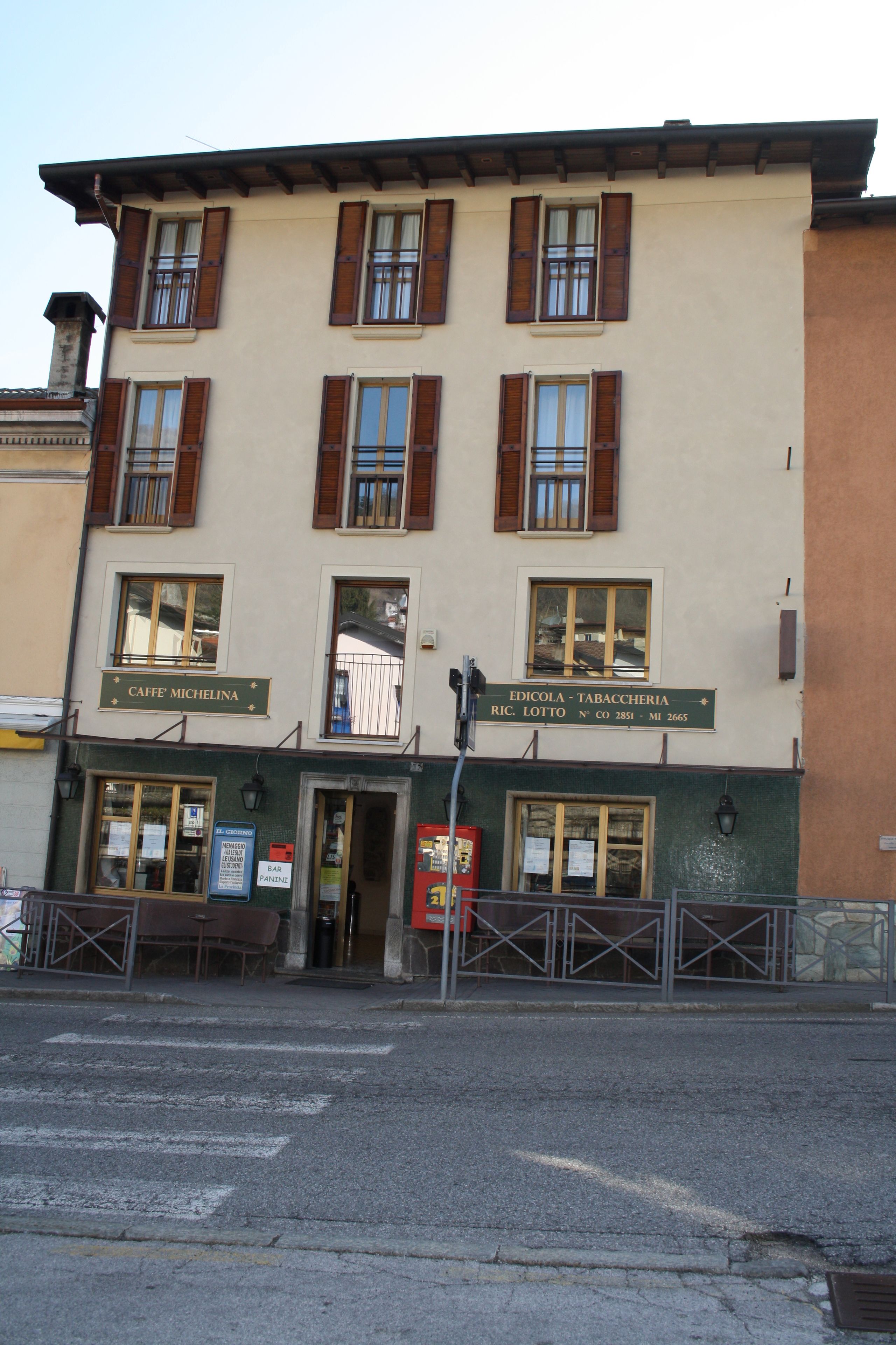 Um edifício com duas lojas no andar térreo, uma delas chamada "CAFFE' MICHELINA" e a outra "EDICOLA - TABACCHERIA".