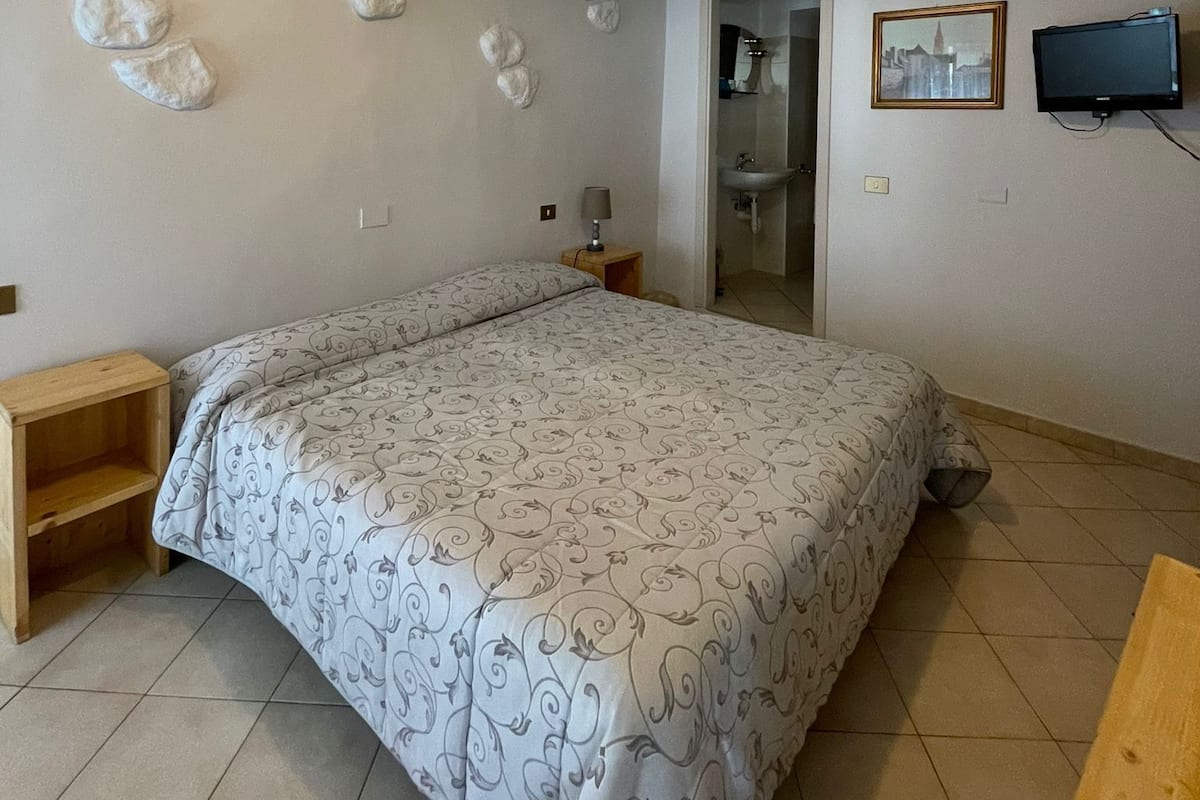 Une chambre à coucher comprenant un lit, une table de chevet, un téléviseur fixé au mur et un luminaire au plafond.