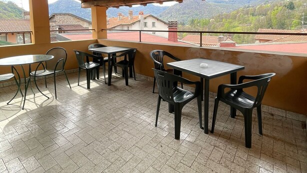 An outdoor patio with wooden beams, tiled flooring, and tables and chairs.